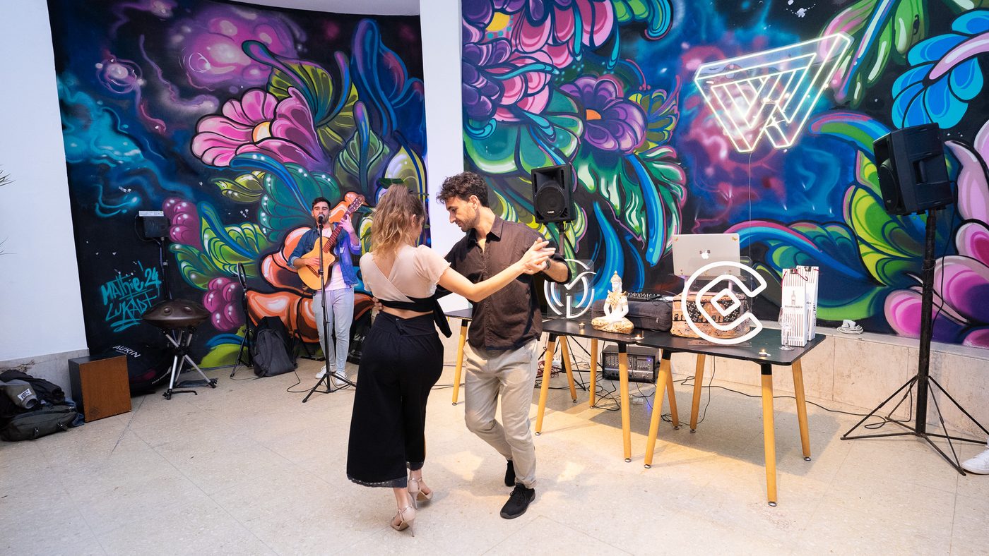 Dos personas bailan durante un encuentro con música en vivo, delante de un mural pintado